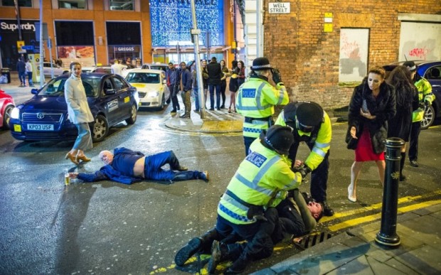 © Licensed to London News Pictures . 01/01/2016 . Manchester , UK . Police detain a man whilst another lies collapsed in the road . Revellers in Manchester on a New Year night out at the clubs around the city centre's Printworks venue . Photo credit : Joel Goodman/LNP
